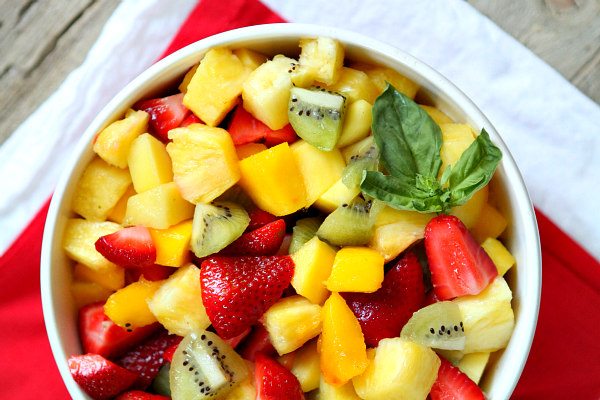 Basil Lime Fruit Salad recipe from RecipeGirl.com #basil #lime #fruit #salad #recipe #RecipeGirl Basil Lime Fruit Salad in a white bowl set on a red cloth napkin