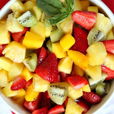 overhead shot of basil lime fruit salad in a white bowl set on a red napkin