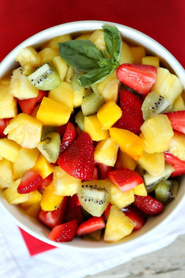 Basil Lime Fruit Salad in a white bowl set on a red cloth napkin. Garnishished with a sprig of fresh basil