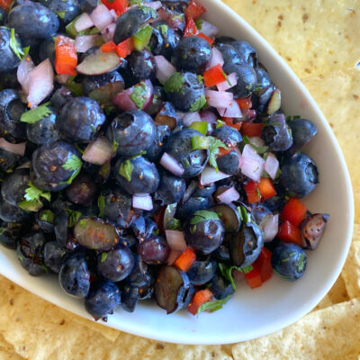 blueberry salsa in a white bowl surrounded by tortilla chips on a white/blue striped napkin