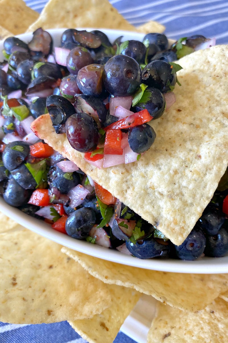 blueberry salsa in a white bowl surrounded by tortilla chips with salsa on one of the chips