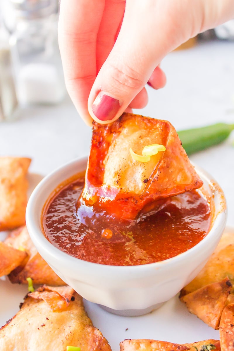 dipping a won ton into bowl of red dipping sauce
