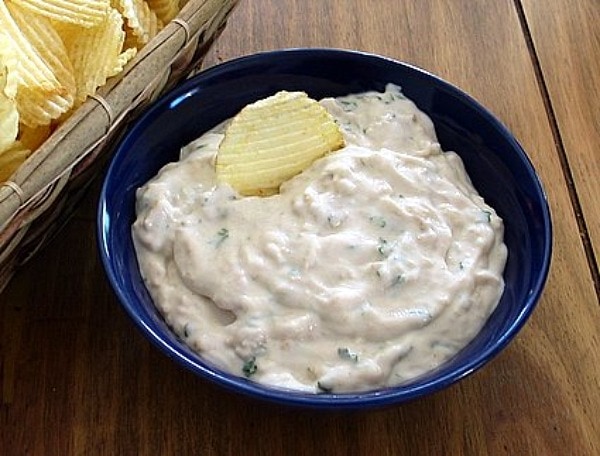 Clam Dip displayed in a royal blue bowl on a wooden table served with potato chips