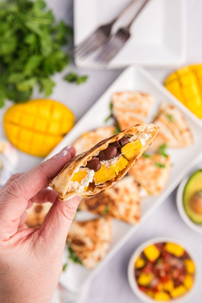 hand holding piece of mango black bean goat cheese quesadilla