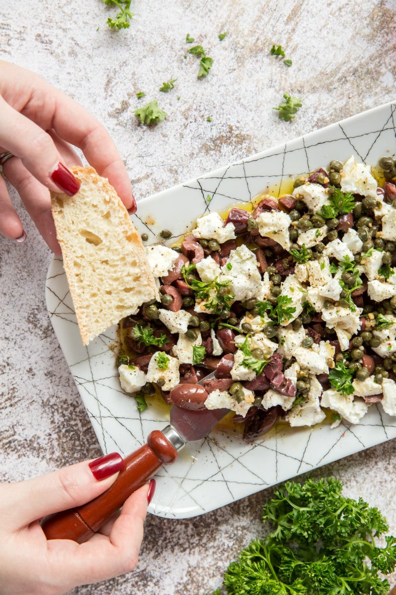 hands serving olive and goat cheese on baguette