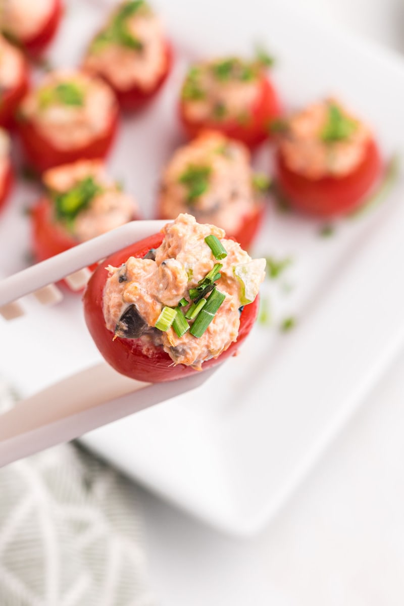 tongs holding salmon stuffed cherry tomatoes