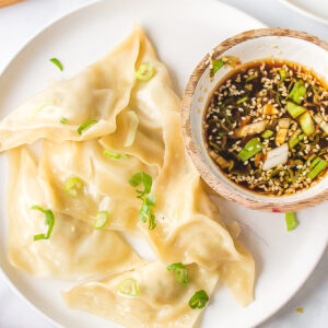 steamed shrimp dumplings on a plat with a bowl of dipping sauce