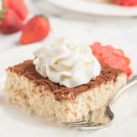 slice of tres leches cake on a white plate with whipped cream and strawberry