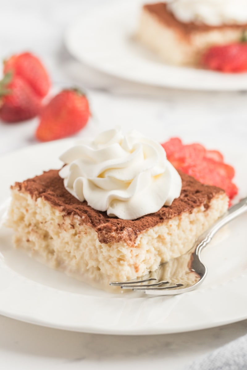 slice of tres leches cake on a white plate with whipped cream and strawberry