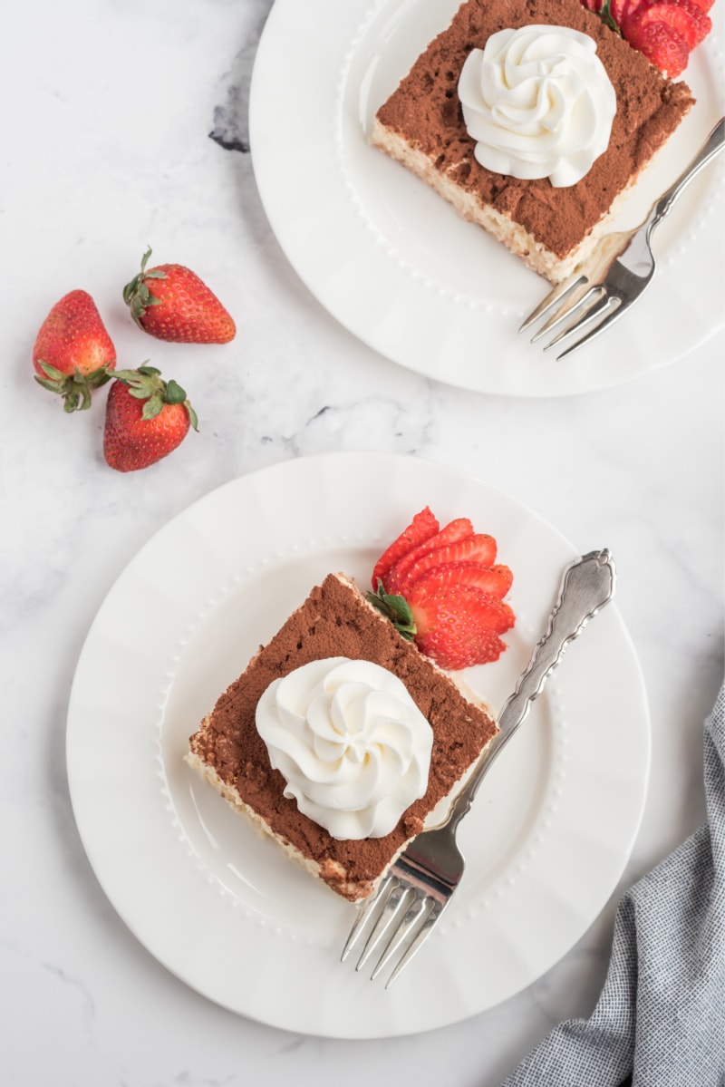 slice of tres leches cake on a white plate with whipped cream and strawberry