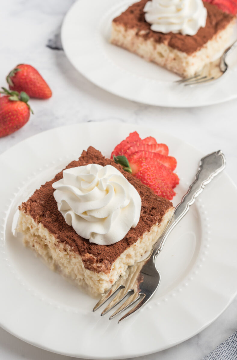 slice of tres leches cake on a white plate with whipped cream and strawberry