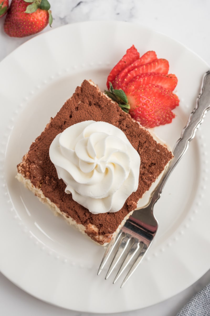 slice of tres leches cake on a white plate with whipped cream and strawberry