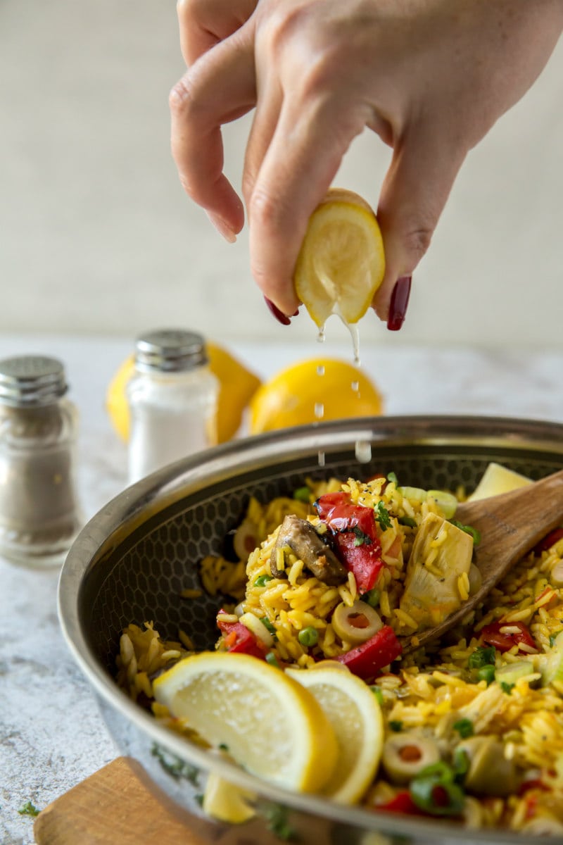 squeezing lemon onto pan of vegetable paella