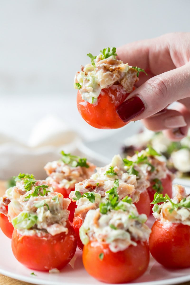 picking up a bacon stuffed cherry tomato above a plate of stuffed cherry tomatoes