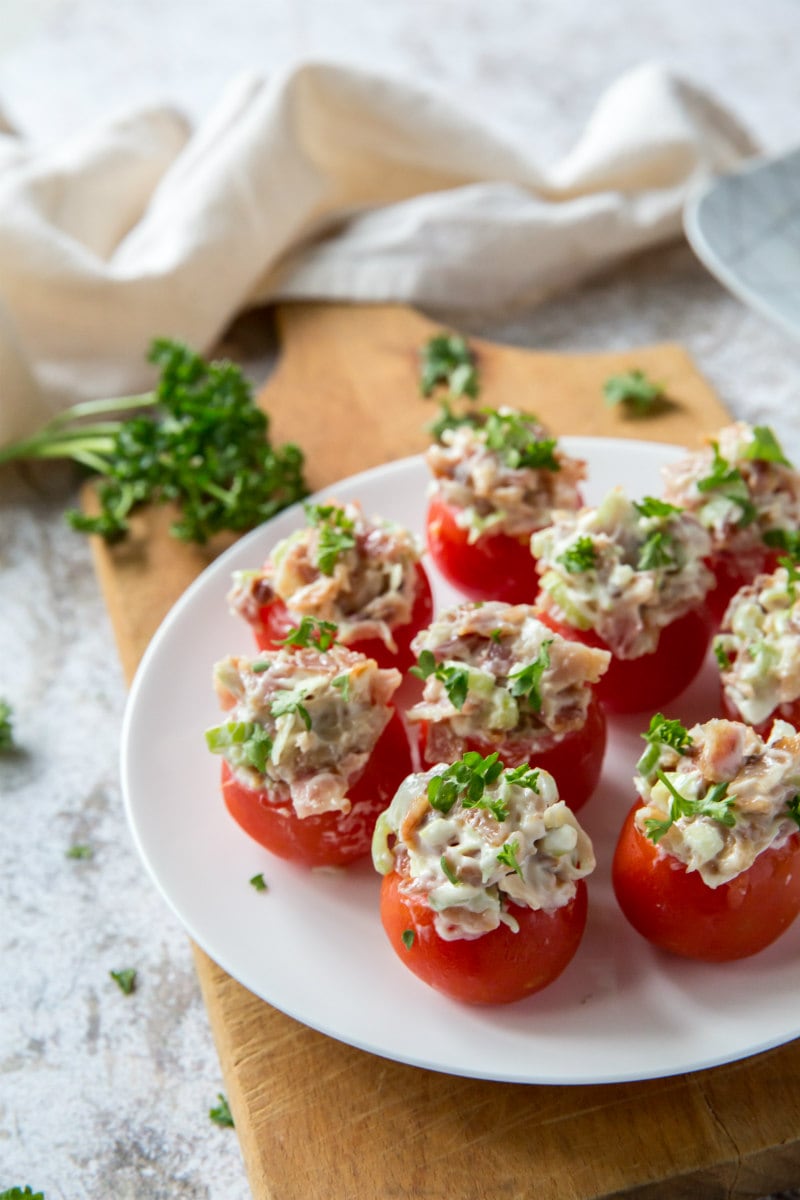 bacon stuffed cherry tomatoes on a white plate sitting on a wooden board with a white napkin in the background