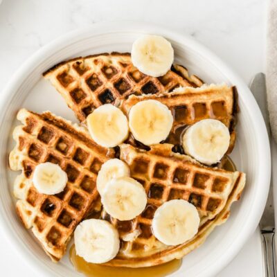 white plate with banana sour cream waffles. Sliced bananas on top