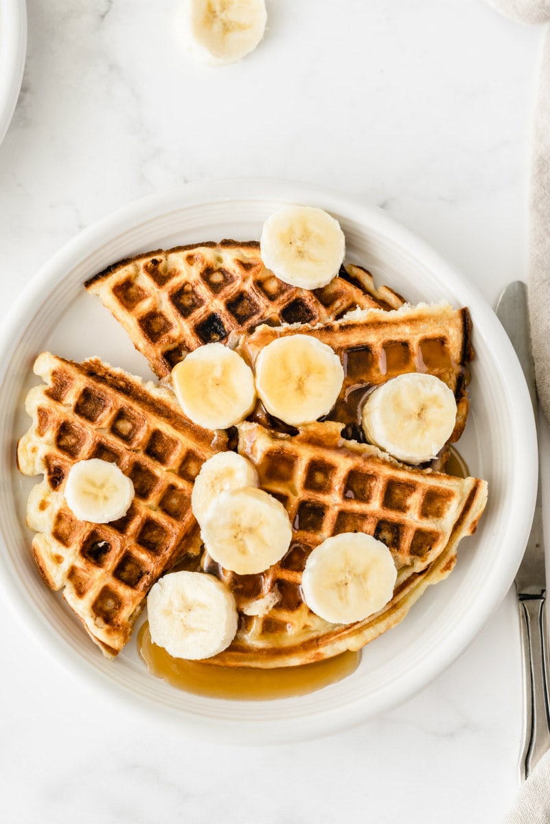 white plate with banana sour cream waffles. Sliced bananas on top