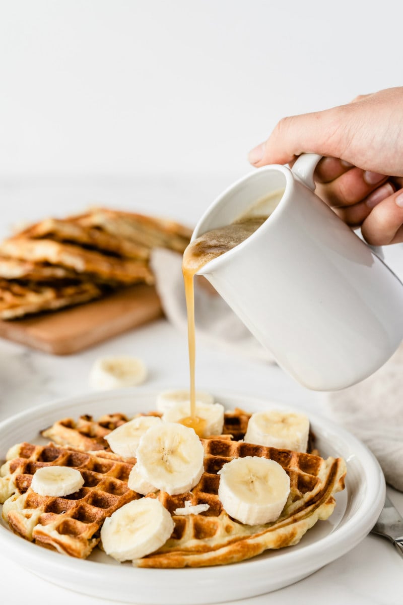 pouring syrup onto banana sour cream waffles with sliced banana on top