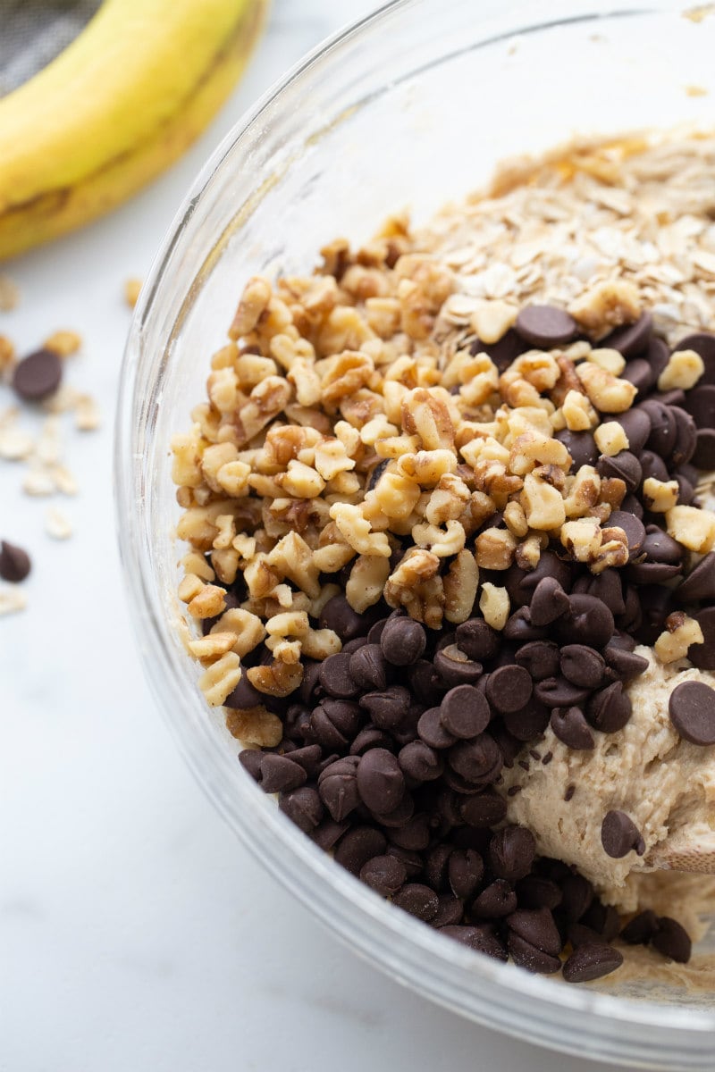 ingredients for banana walnut cookies in a glass bowl ready to be mixed together with a peek or a banana in the background