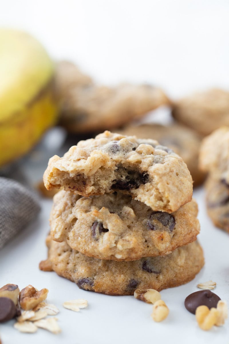 three stacked banana walnut chocolate chip cookies with peek of a banana in the background