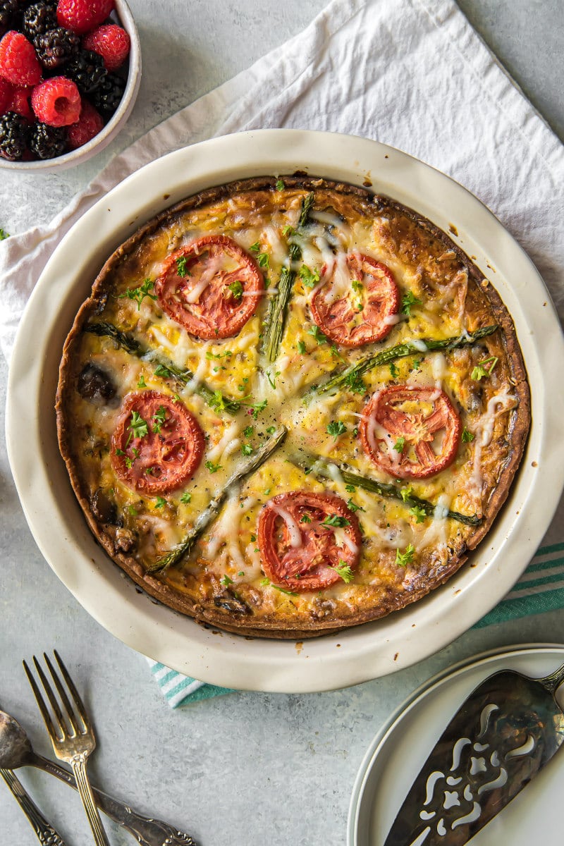 overhead shot of garden vegetable quiche on a white napkin with forks and a bowl of fresh berries on the side