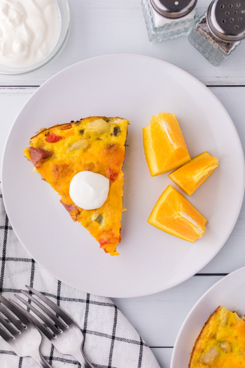 slice of frittata on plate topped with sour cream and oranges on side