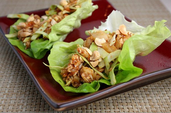 Two Sweet and Spicy Chicken Lettuce Wraps on a burgundy plate set on a woven place mat