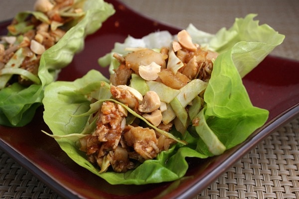 Two Sweet and Spicy Chicken Lettuce Wraps on a burgundy plate set on a woven place mat