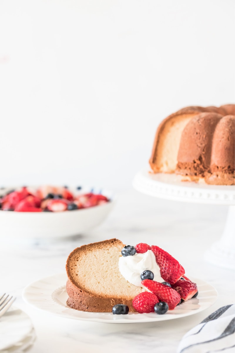 slice of pound cake on white plate with whipped cream and berries