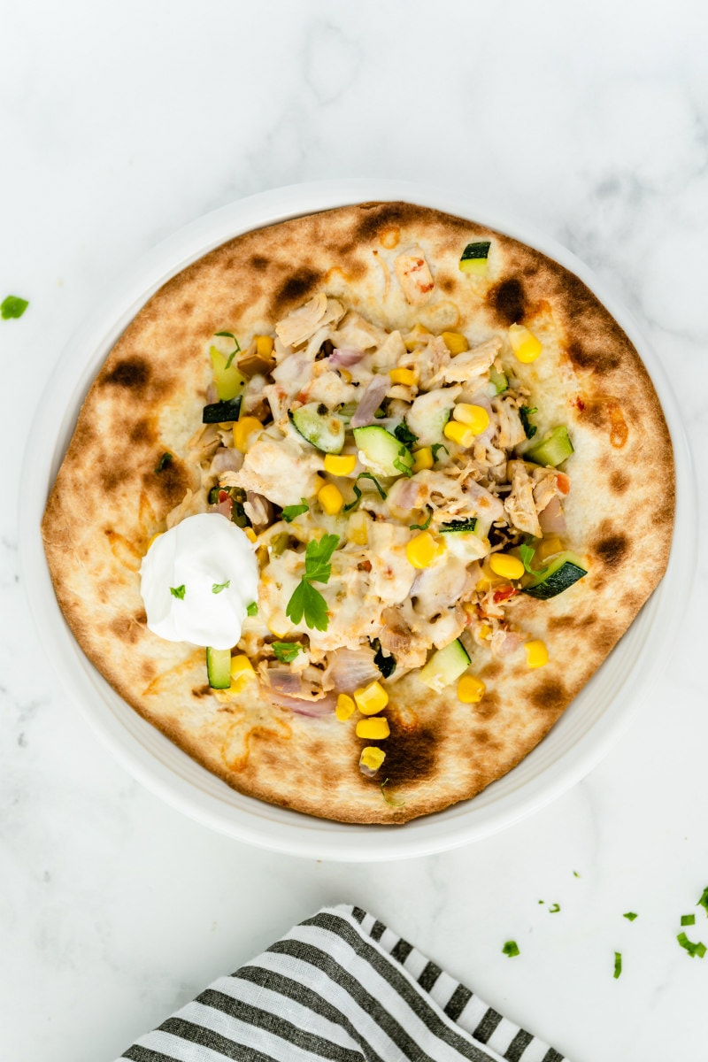 overhead shot of a chicken and summer vegetable tostada with a blue and white striped napkin peeking into the bottom of the photo