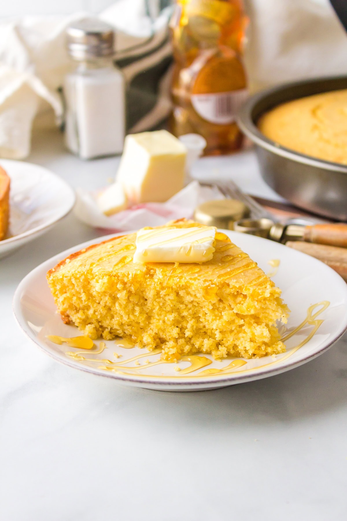 Sweet, moist, and buttery — this easy sweet cornbread recipe is the ultimate comfort side for chili, soups, and BBQ. Ready in under 30 minutes! Moist slice of cornbread on plate with butter and honey on top