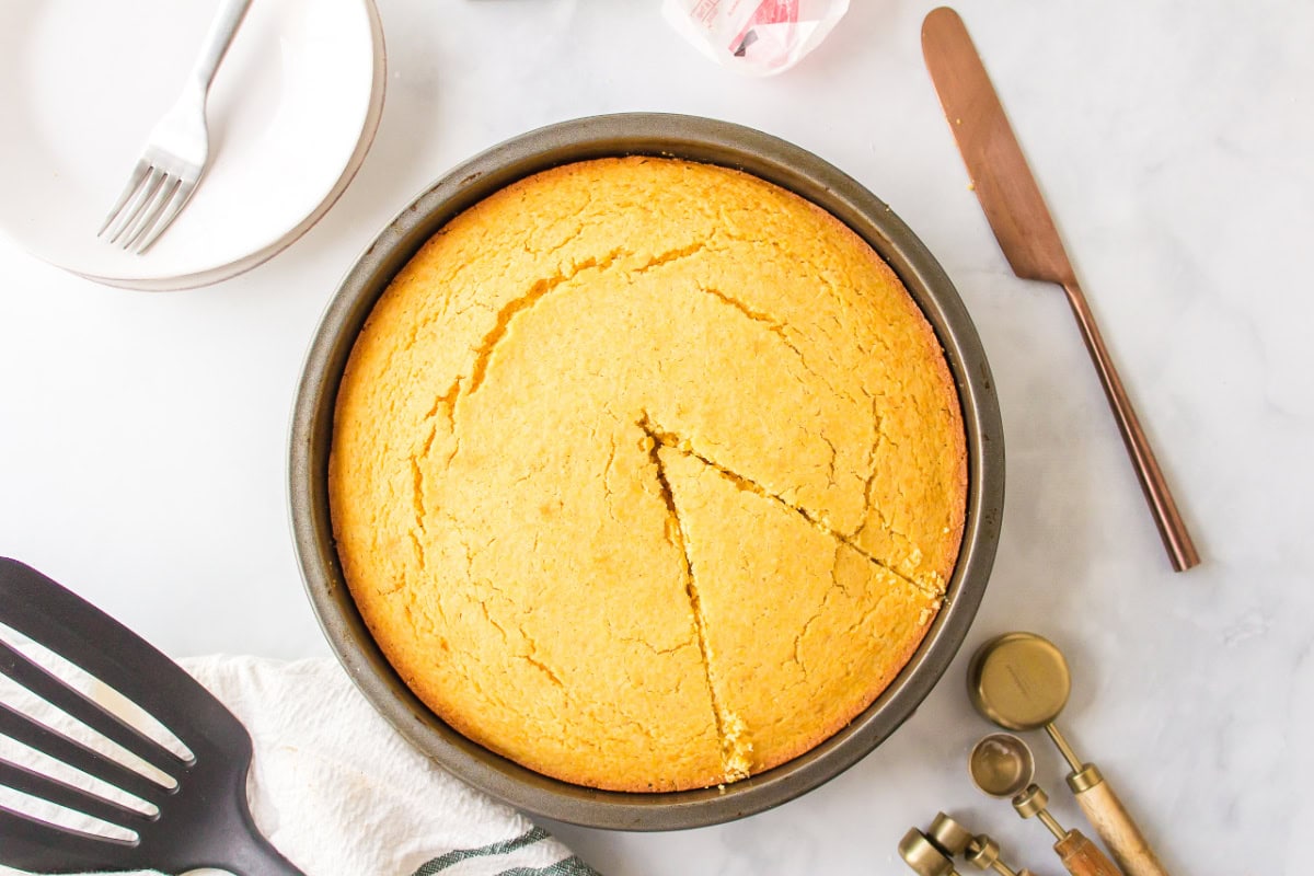Sweet, moist, and buttery — this easy sweet cornbread recipe is the ultimate comfort side for chili, soups, and BBQ. Ready in under 30 minutes! Sweet cornbread in a round pan with piece cut