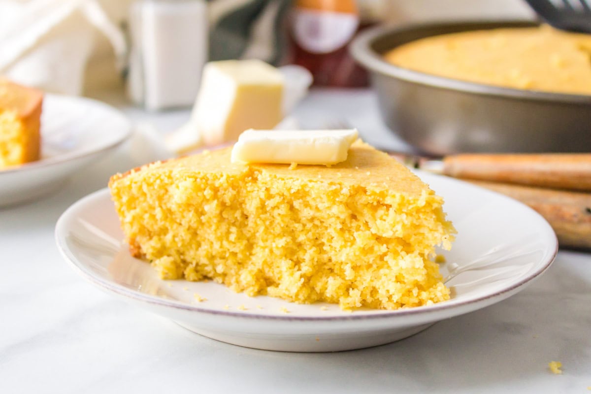 Sweet, moist, and buttery — this easy sweet cornbread recipe is the ultimate comfort side for chili, soups, and BBQ. Ready in under 30 minutes! Moist slice of cornbread on a plate