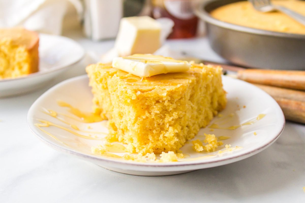 Sweet, moist, and buttery — this easy sweet cornbread recipe is the ultimate comfort side for chili, soups, and BBQ. Ready in under 30 minutes! Golden cornbread on a plate with bite taken out of it