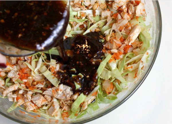 Pouring sauce into the Filling for Sweet and Spicy Chicken Lettuce Wraps in a glass bowl