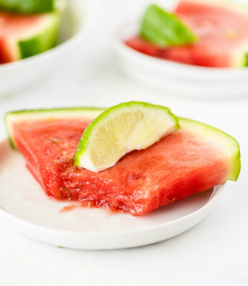 watermelon wedge on a white plate with a bite taken out of it and a lime wedge on top