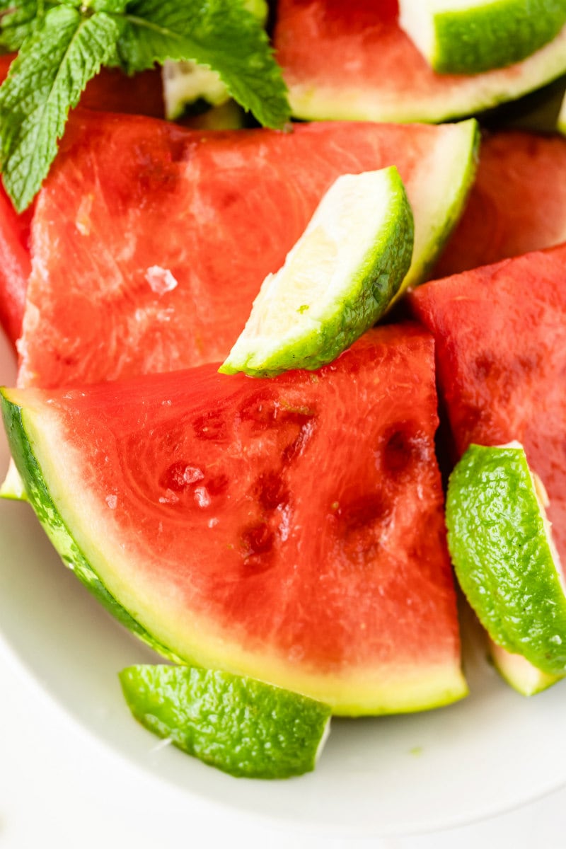 wedges of watermelon soaked with tequila on a white platter with lime wedges