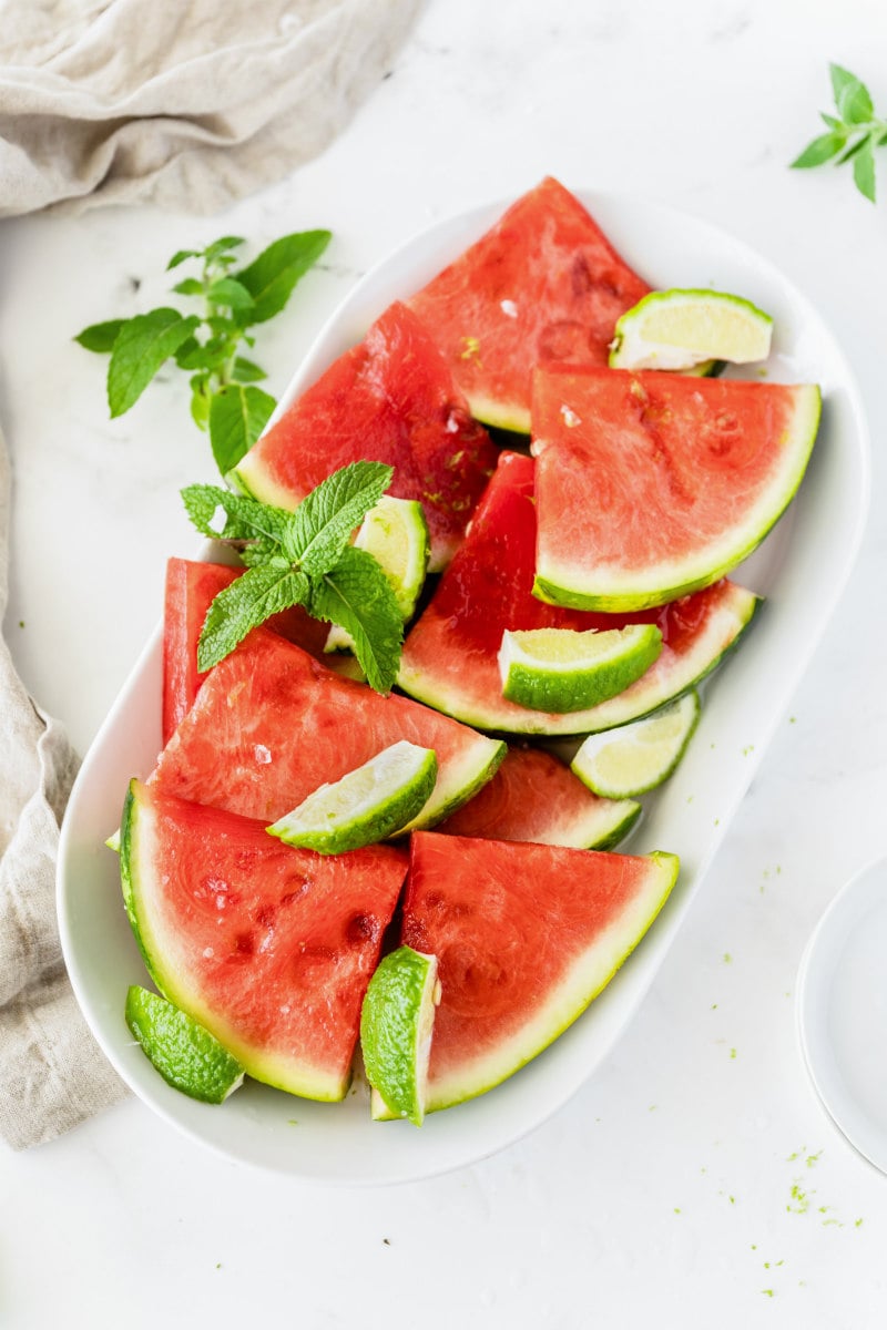 white platter with tequila watermelon wedges, lime wedges and fresh mint