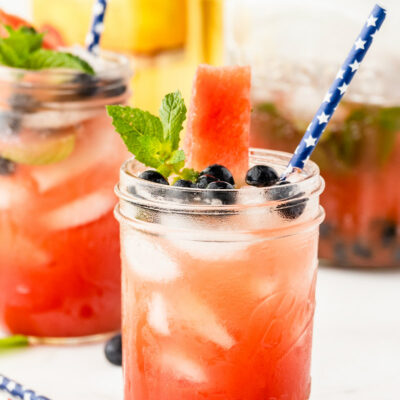 watermelon tequila cocktails in mason jars garnished with fresh blueberries and mint. striped straws. bottle of tequila in the background