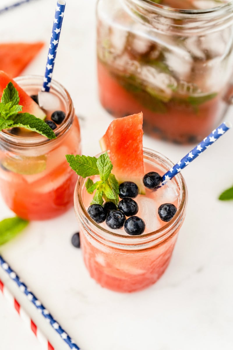 watermelon tequila cocktails in mason jars. garnished with blueberries and fresh mint and watermelon wedges. striped straws.