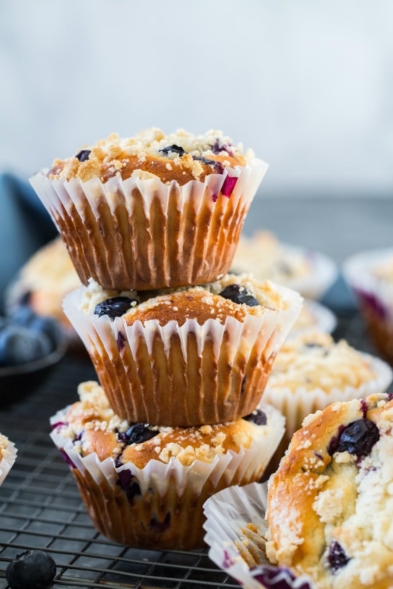 three blueberry muffins stacked with more blueberry muffins in the background