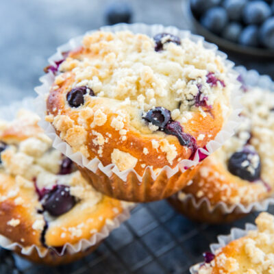 blueberry muffin sitting on top of other blueberry muffins with fresh blueberries in the background