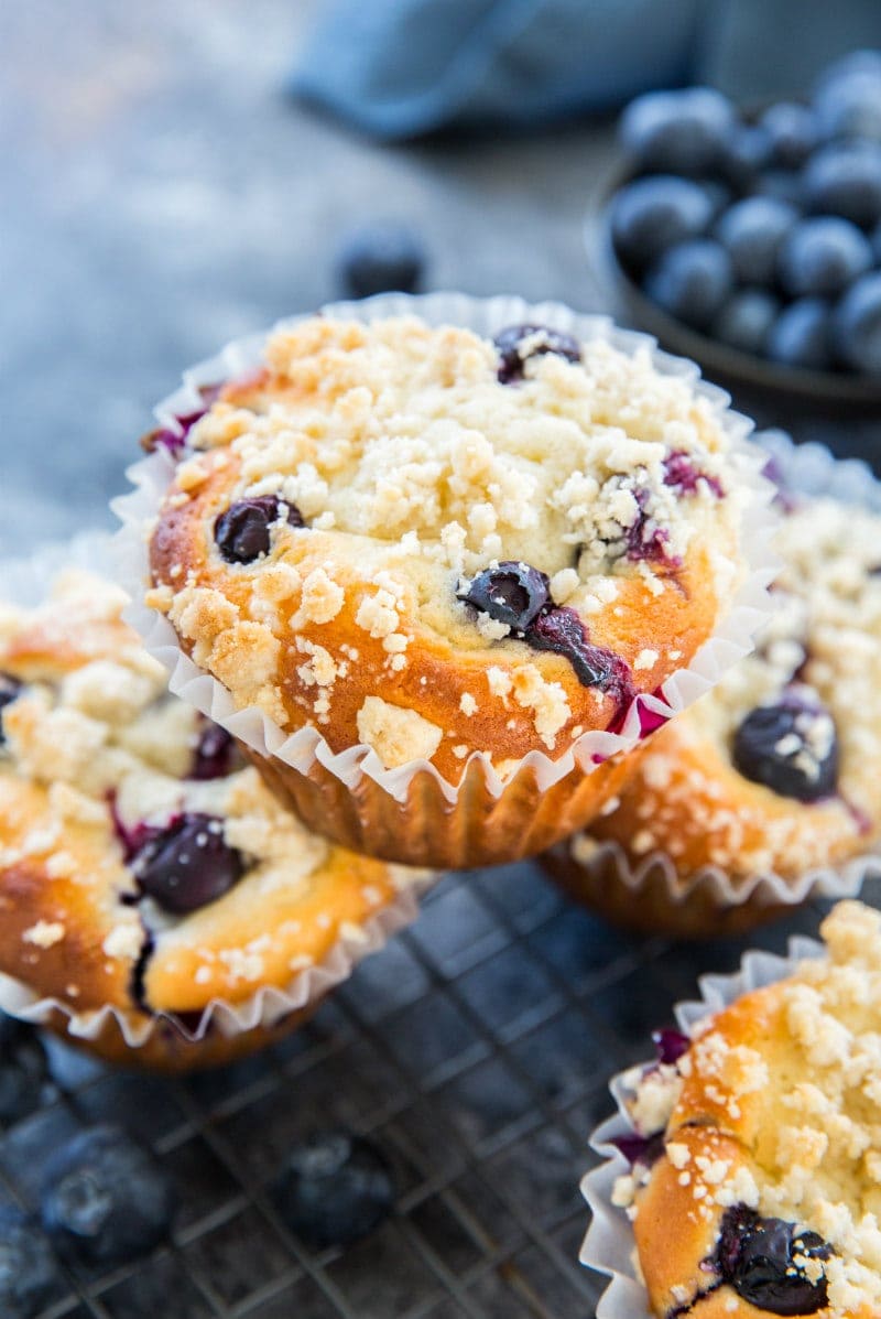 blueberry muffin sitting on top of other blueberry muffins with fresh blueberries in the background