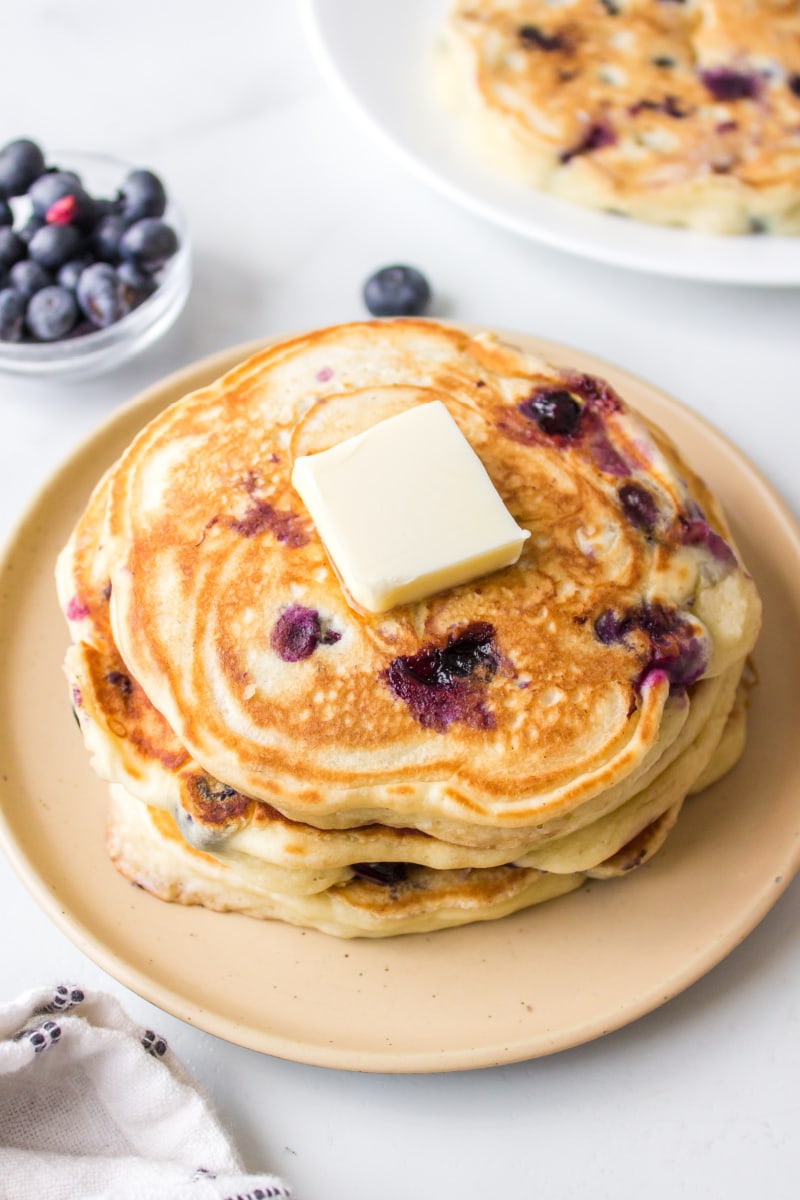 blueberry pancakes stacked on plate with pat of butter on top