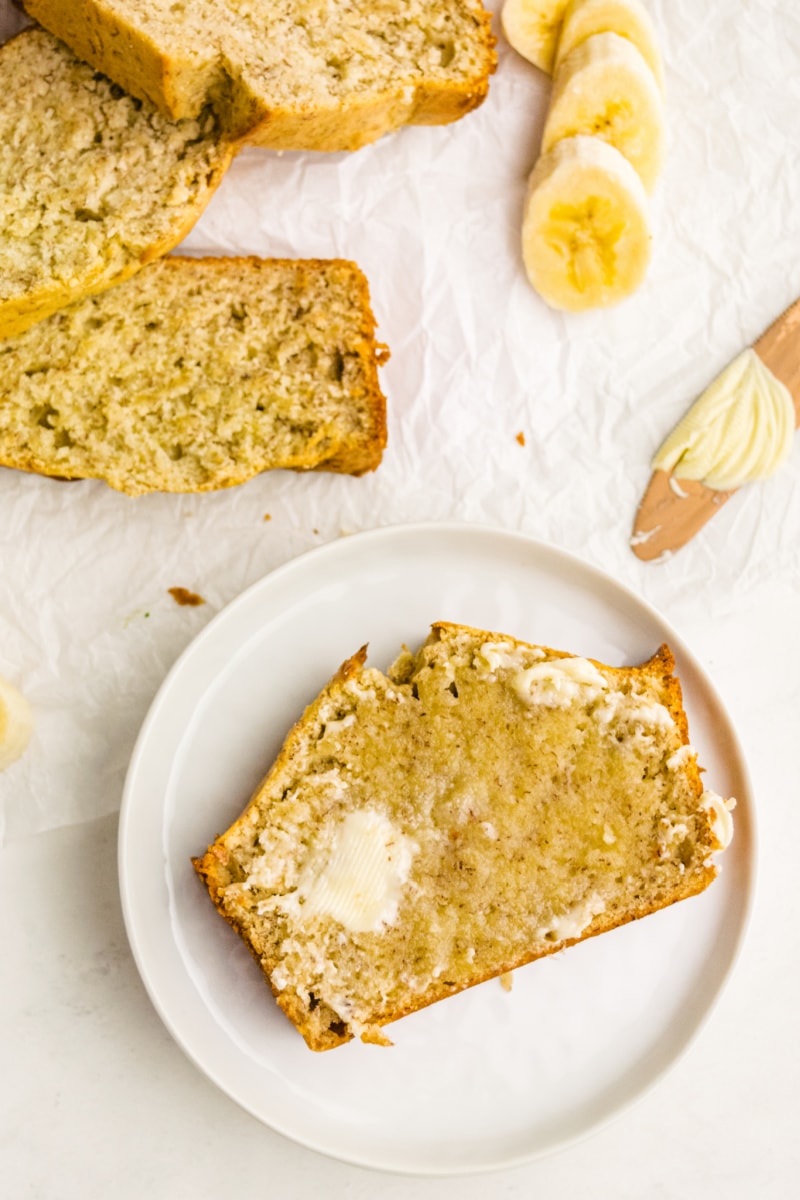 slice of banana bread on white plate with melting butter