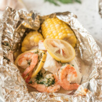 grilled new england seafood foil packets opened up to see the inside. fresh herbs in background