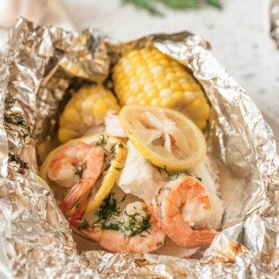 grilled new england seafood foil packets opened up to see the inside. fresh herbs in background
