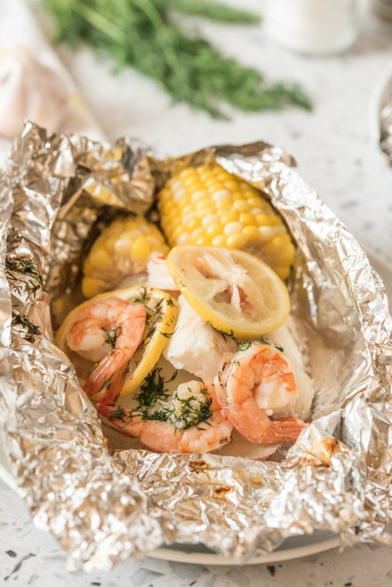 grilled new england seafood foil packets opened up to see the inside. fresh herbs in background