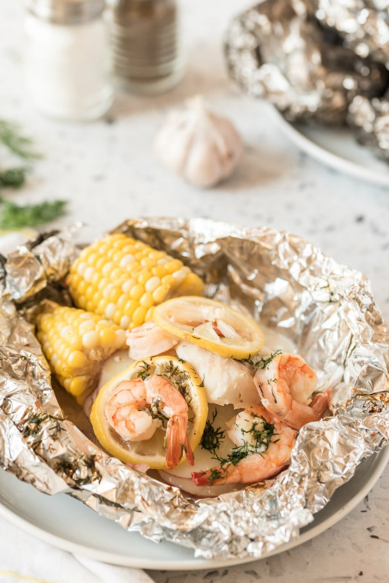 grilled new england seafood foil packets opened up to see the inside. salt and pepper and garlic in the background