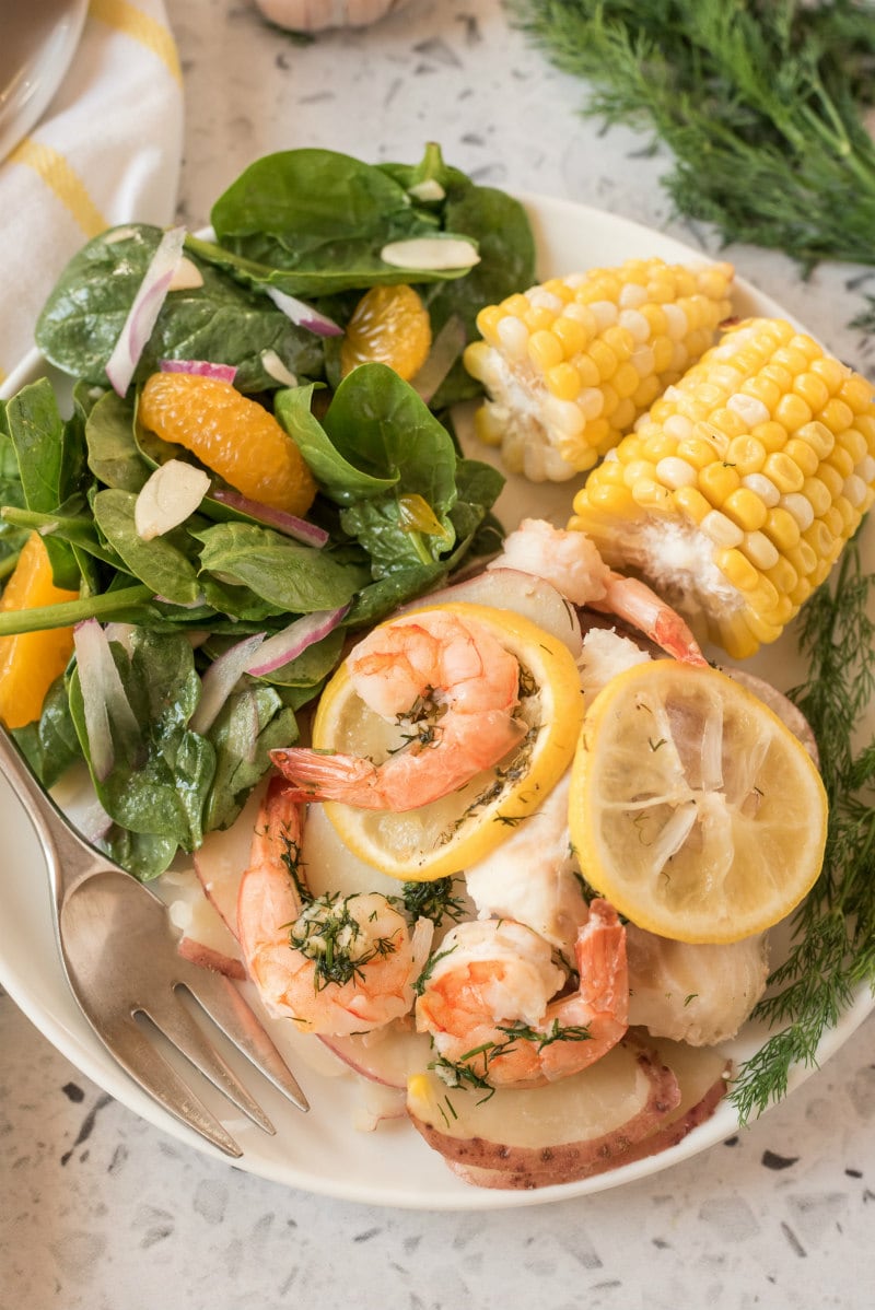 seafood and corn on a white plate with salad and a fork